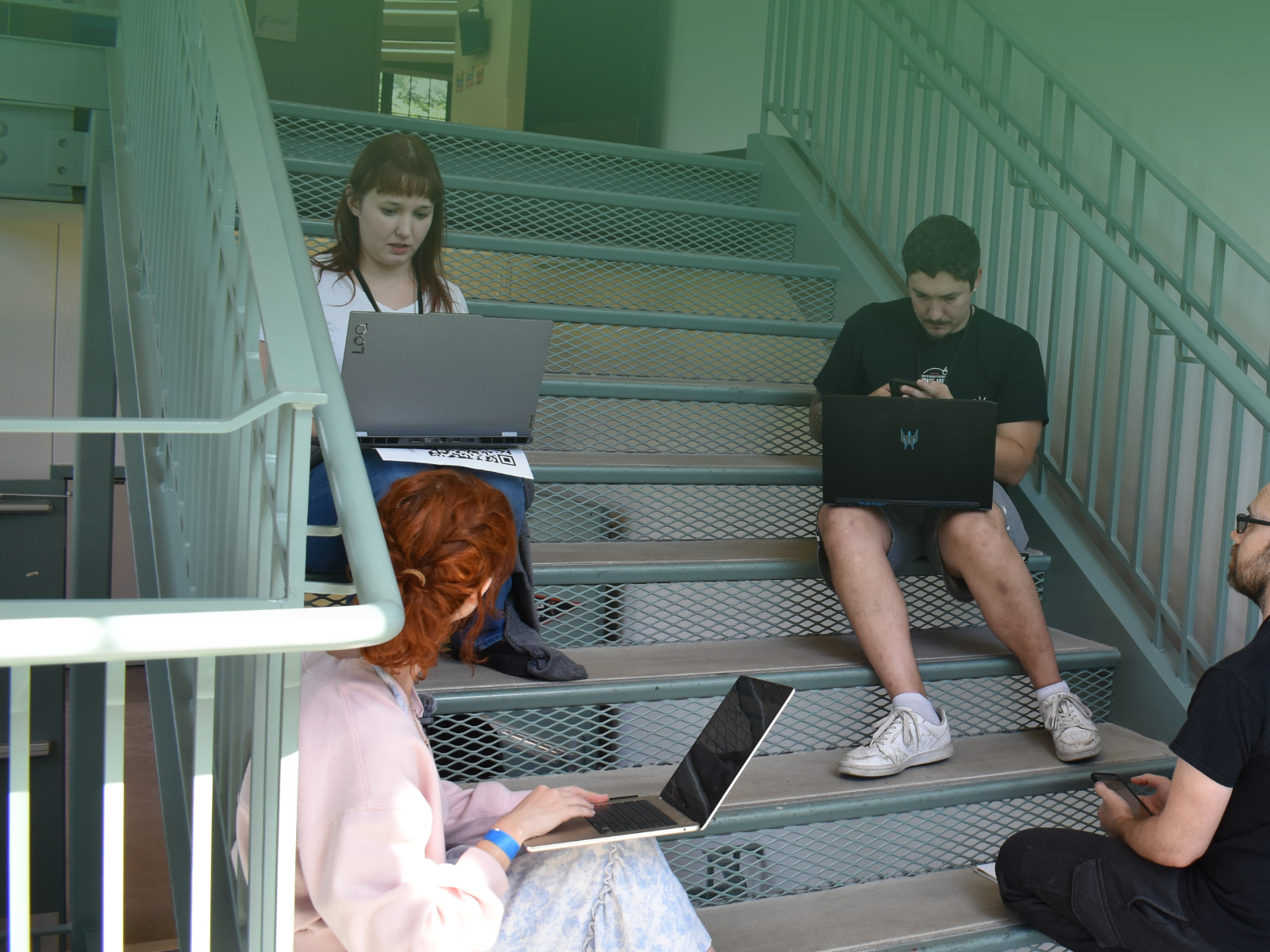 Students collaborating with laptops in a campus stairwell